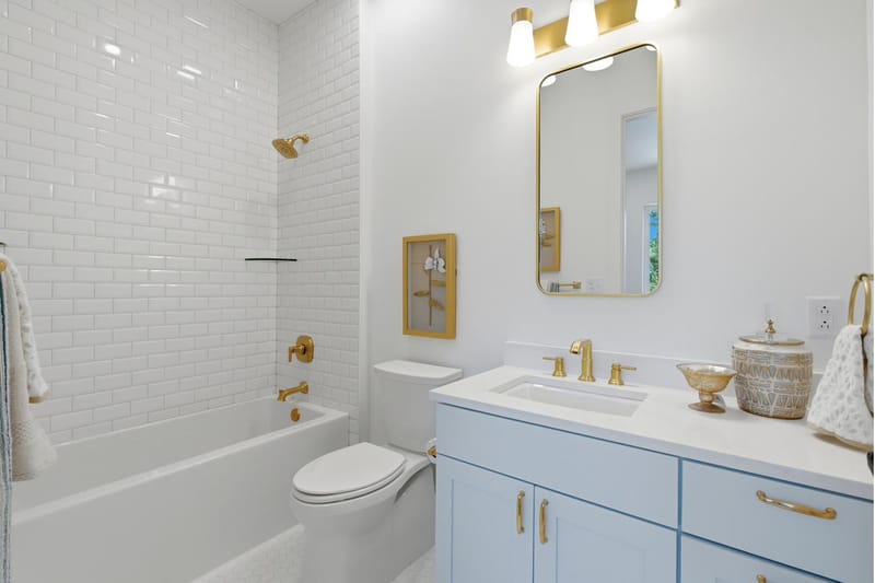 Guest bath with a subway-tile tub surround, brass fixtures, and a pale blue vanity