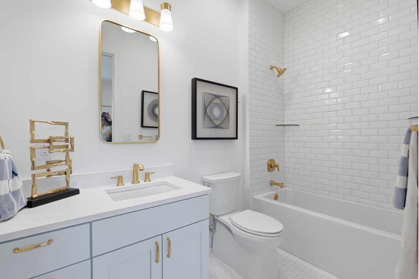 Guest bath at The Breakaway Oxford with a tub and shower, brass sconces, and a pale blue vanity