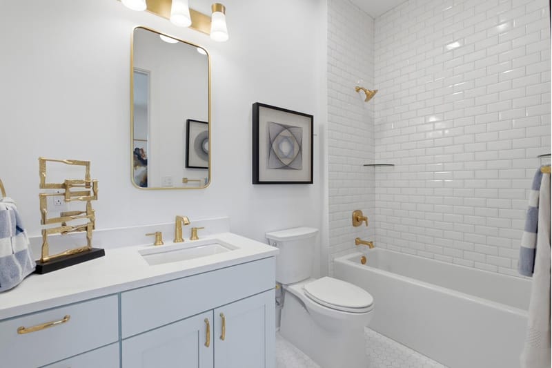 Guest bath with a tub and shower, brass sconces, and a pale blue vanity